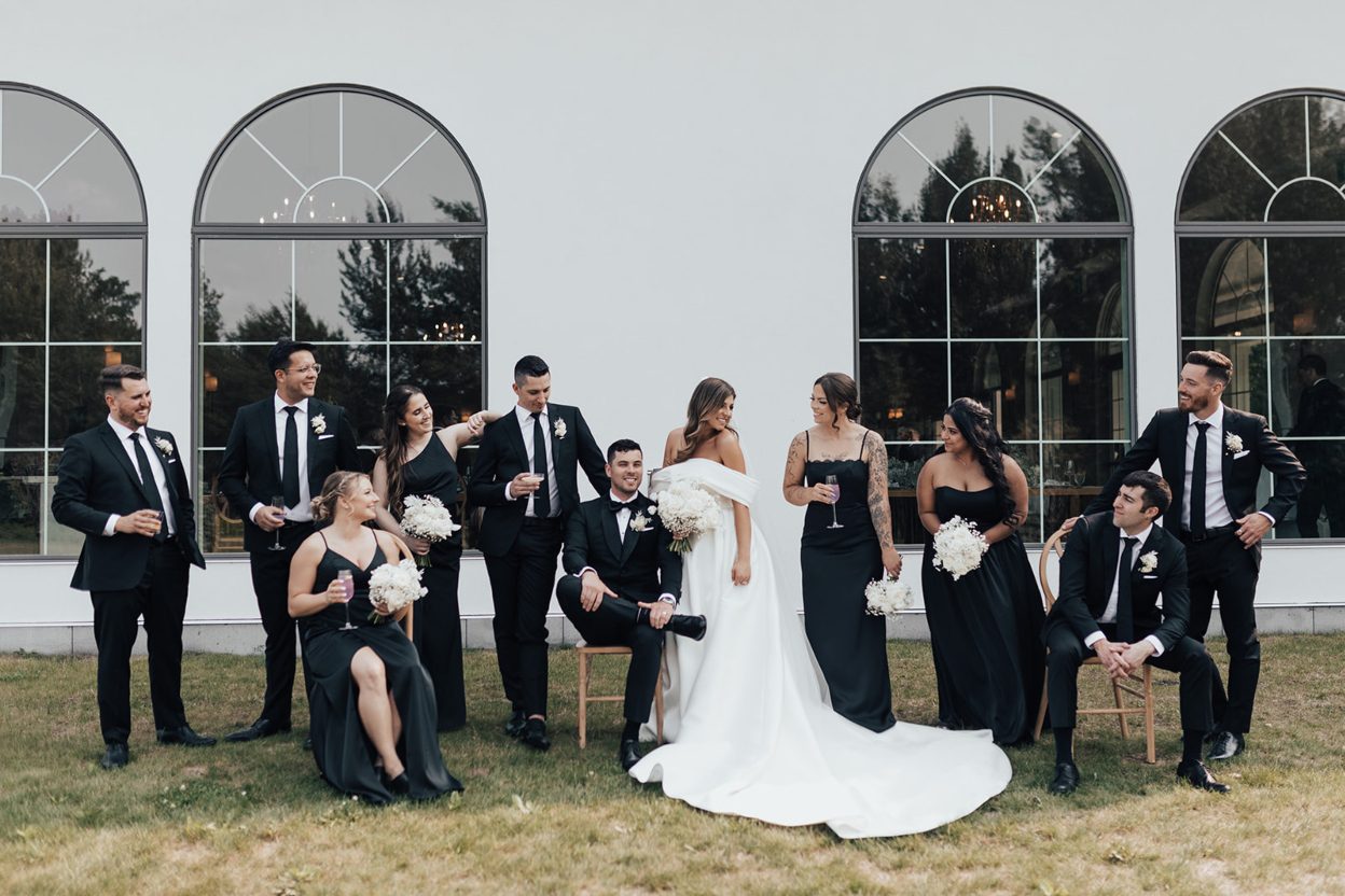 Wedding Party The wedding party outside in front of arched windows, some seated and some standing as they look at each other laughing and smiling.