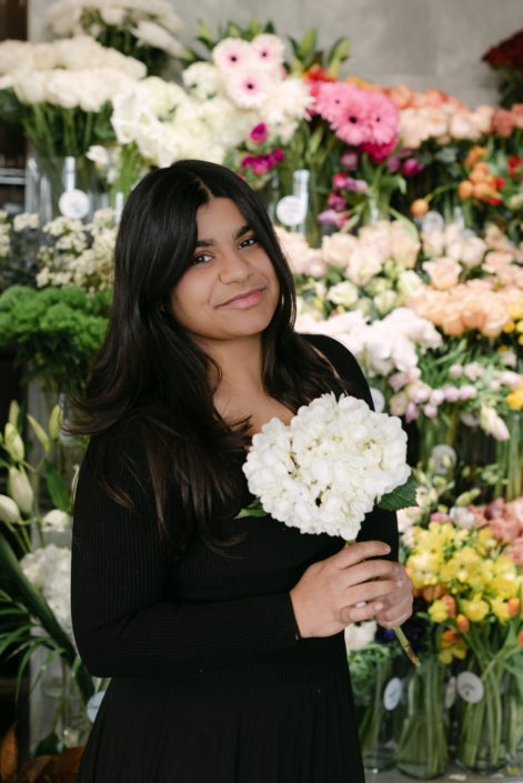 New Calyx staff member, Zulekha looks at the camera with a soft smile as she holds a beautiful white hydrangea close to her chest.