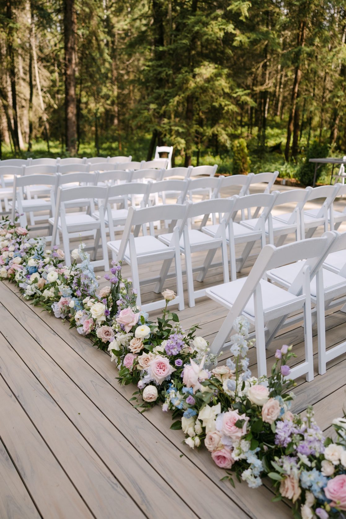 Neat rows of white chairs at the ceremony, with a neat line of beautiful pastel arrangements lining the aisle.