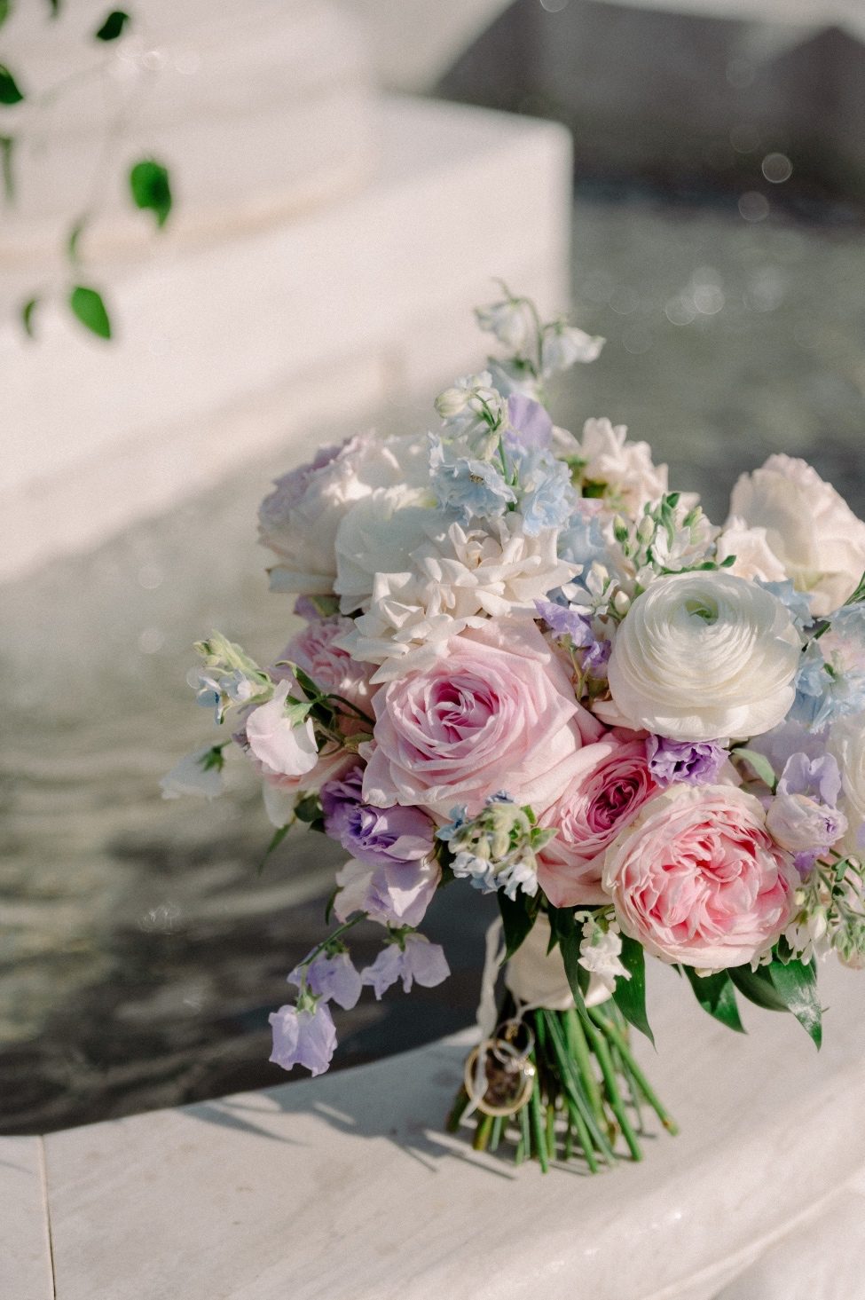 Bridal bouquet of roses, sweet peas, delphinium, lisianthus, ranunculus and tweedia on the edge of the fountain.