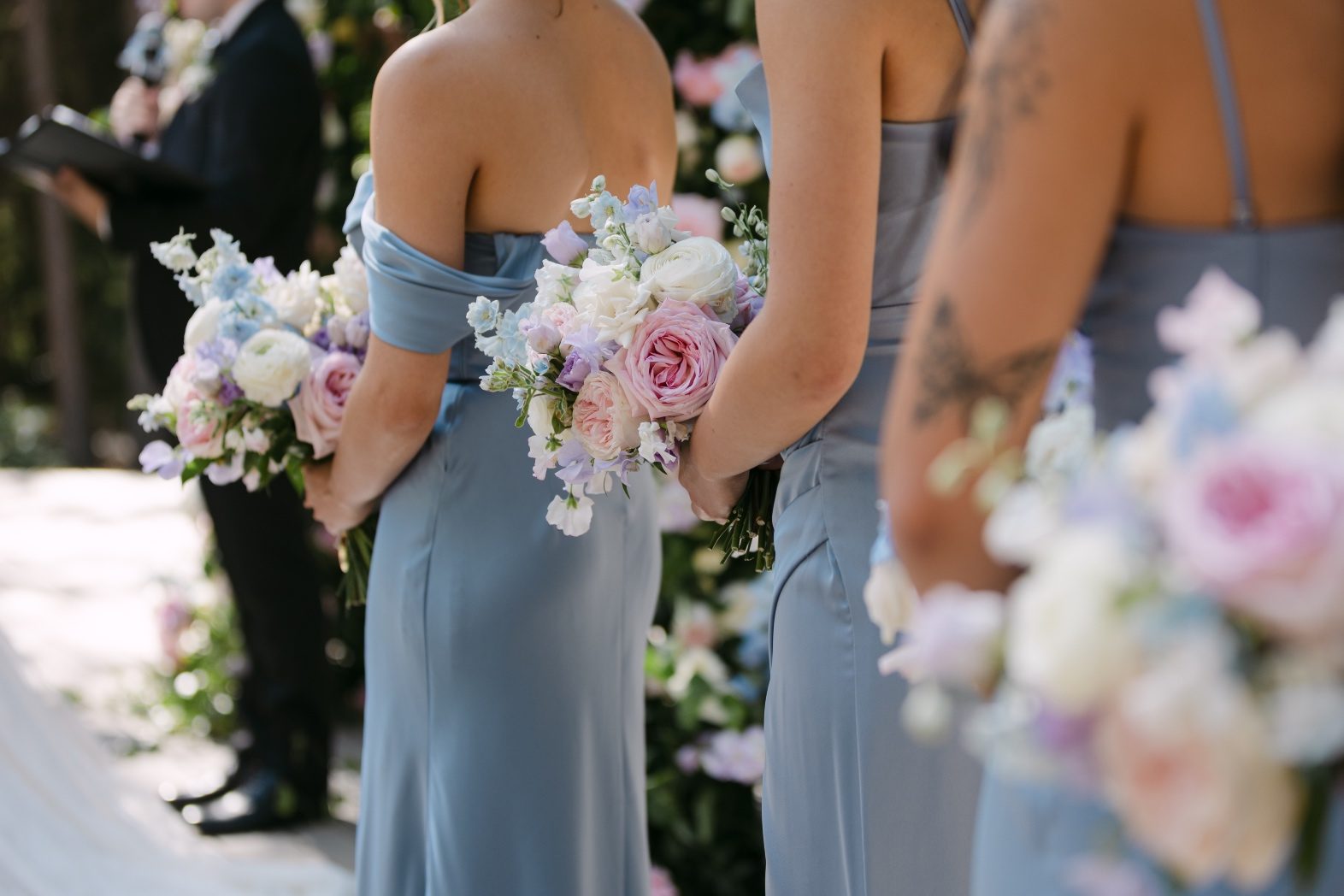 View from behind the bridesmaids standing in a line, in their pretty powder blue dresses, and holding their pastel bouquets.