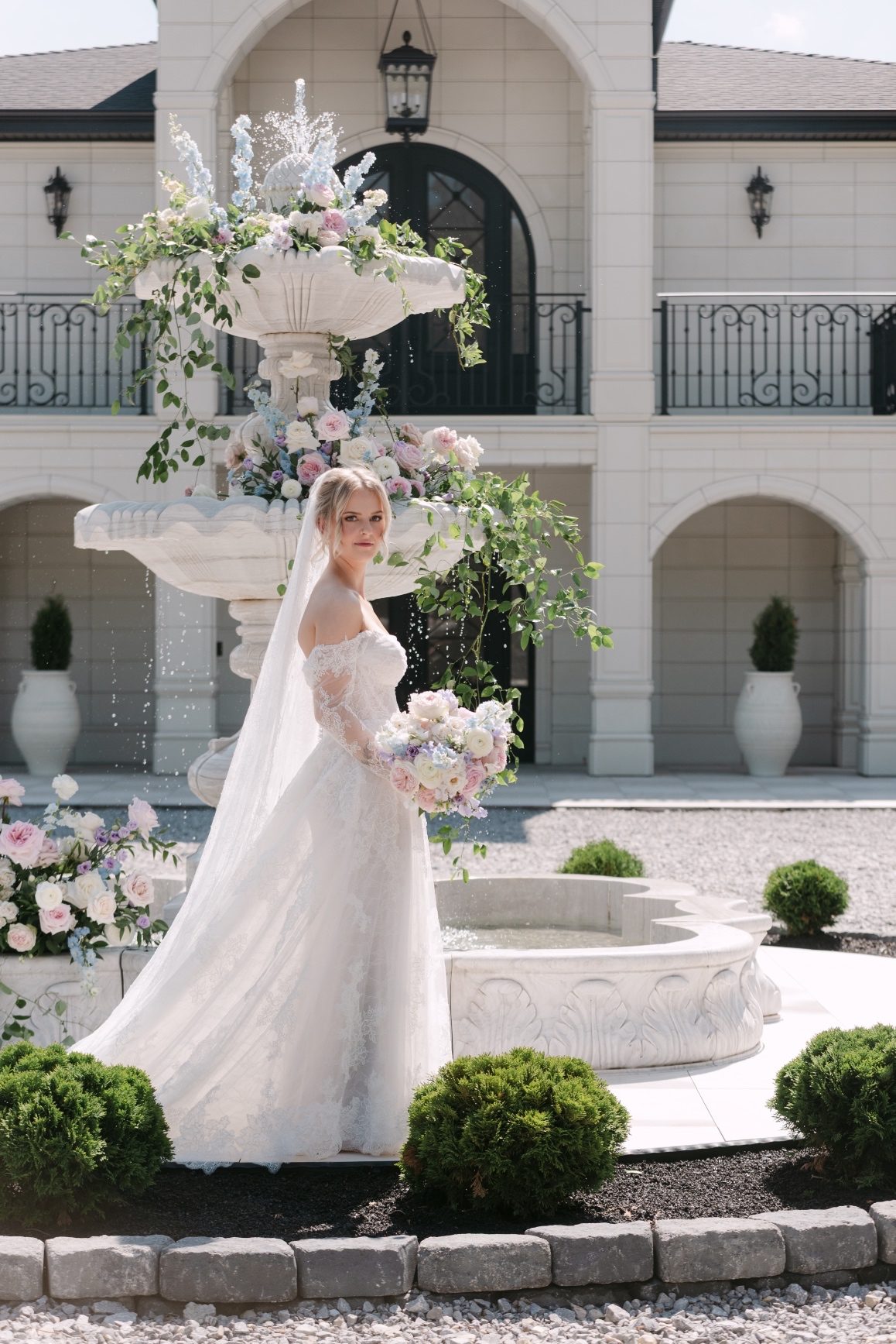 Kaylee stands in front of the fountain, her body turned to the side and you can see the sunlight coming through some of the layers of her dress and veil as she looks at the camera.