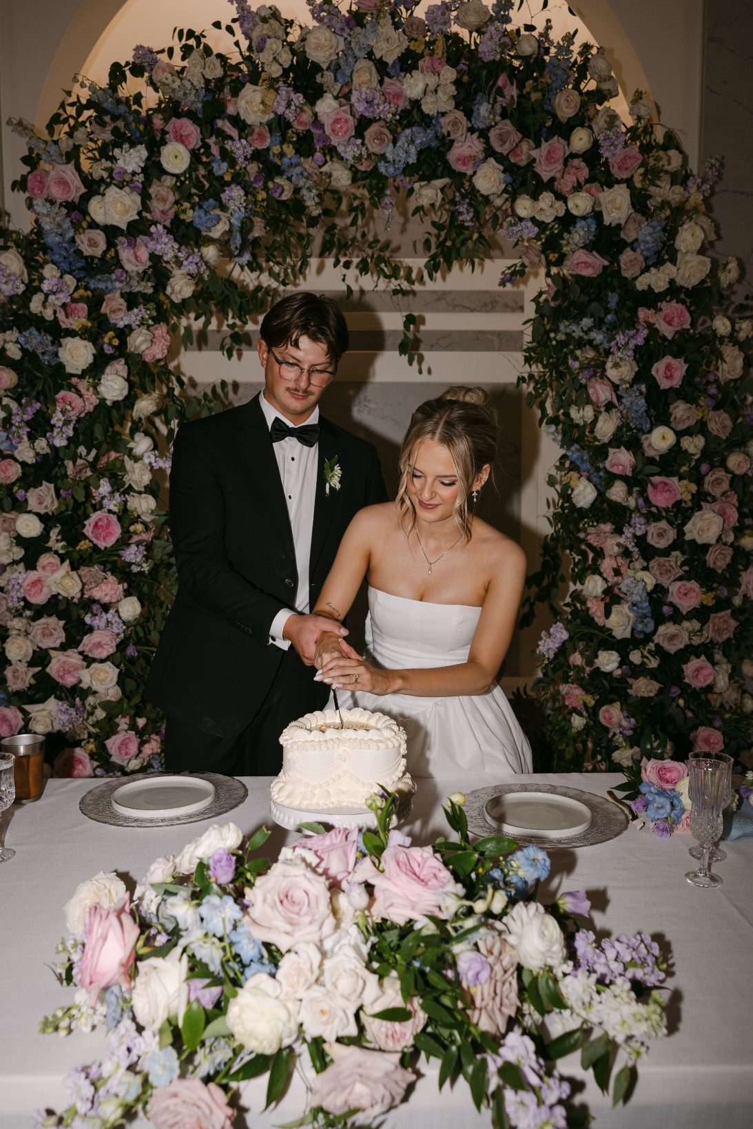 Cutting Cake Later in the reception, Kaylee has changed into her second dress, she stands with Oran behind the sweetheart table as they cut a heart shaped wedding cake together.