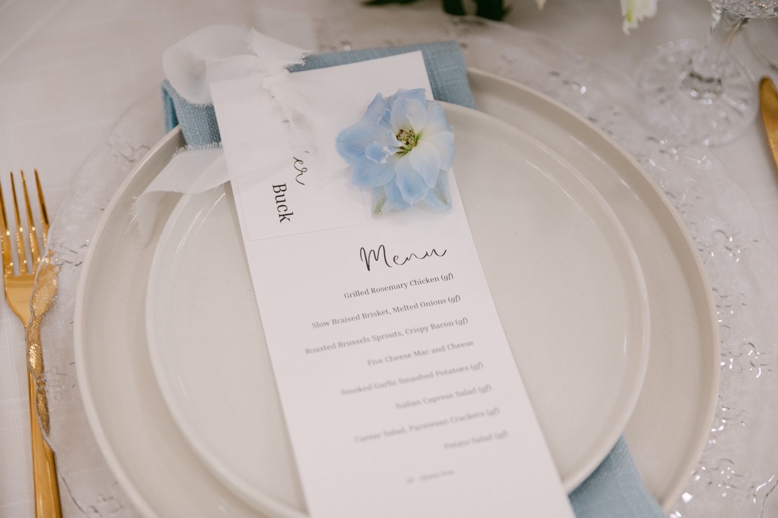 Close up of the menu cards with an individual blue delphinium bloom, to compliment the blue linens beautifully.