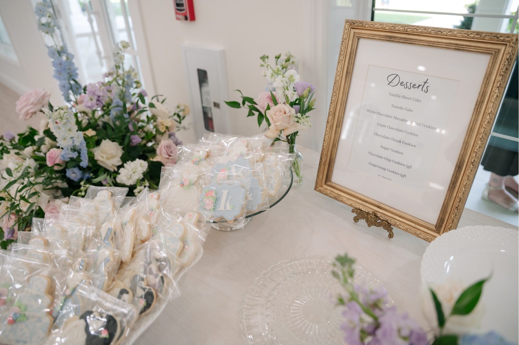 An assortment of cookies and desserts at the dessert bar with a simple pastel arrangements and groupings of bud vases.