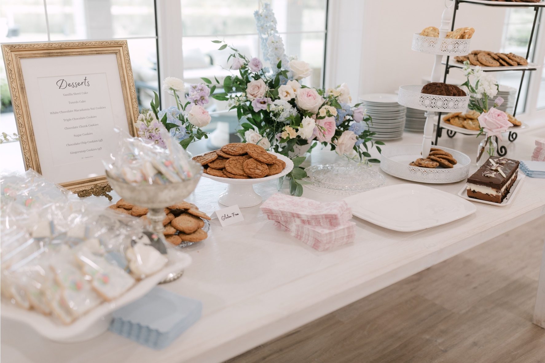 A yummy looking dessert bar with an assortment of cookies and treats, with a pastel arrangement and groupings of bud vases.