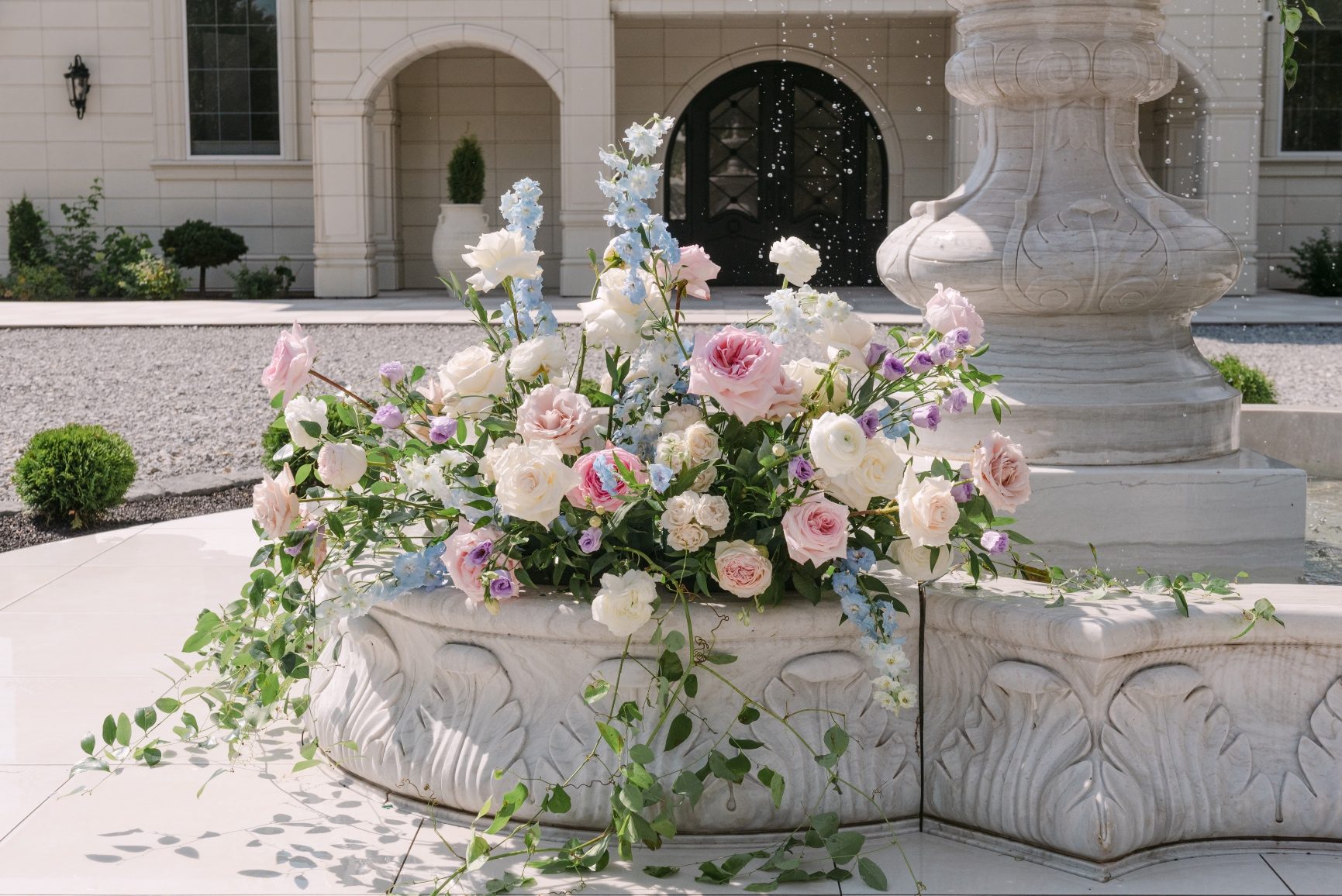 The pastel arrangement at the base of the fountain, with vining greens pooling below it, and pretty, gardeny blooms arranged in an organic fashion.