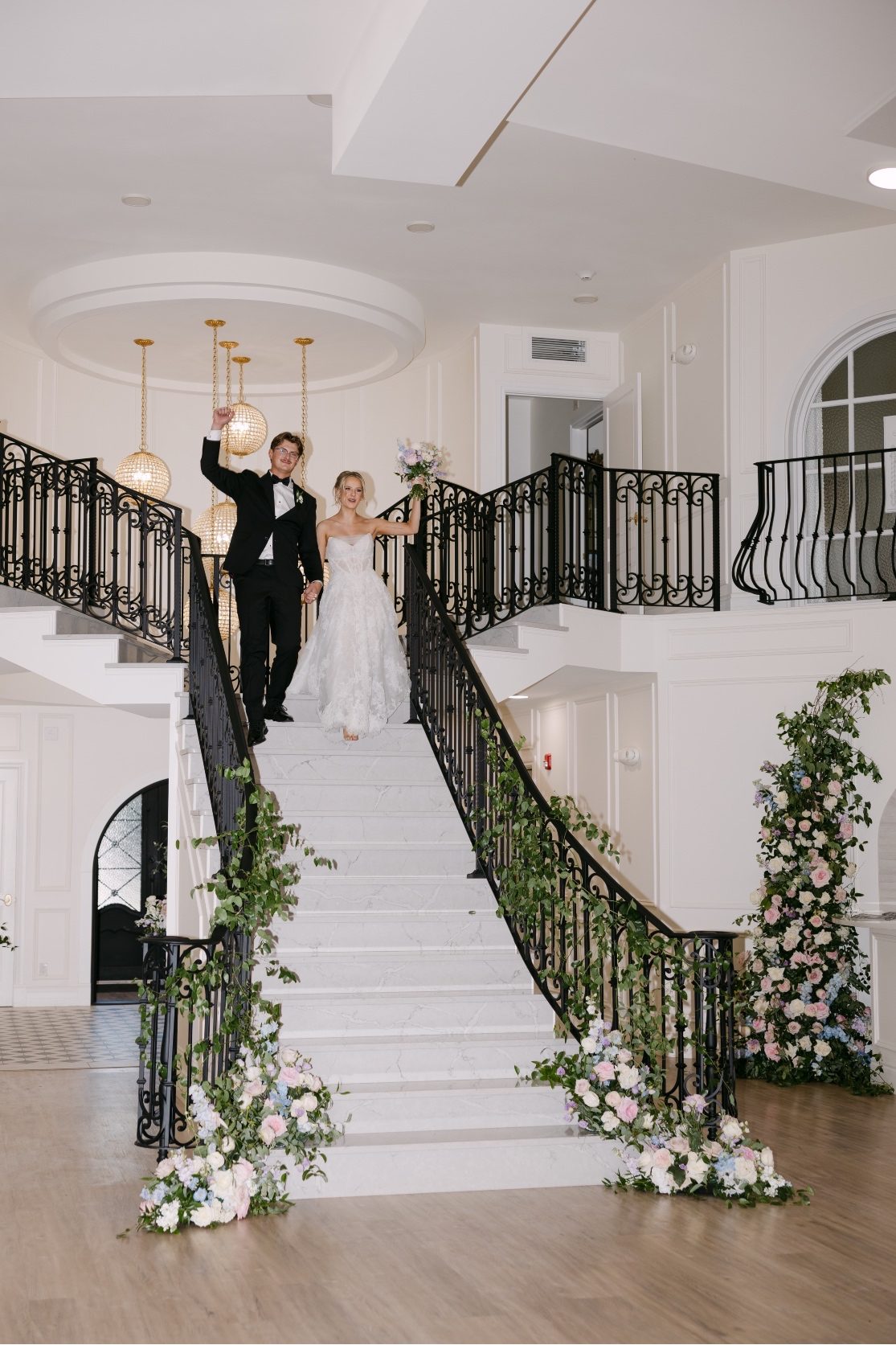 Kaylee and Oran at the top of the staircase, arms raised in celebration as they make their way down to greet their guests.