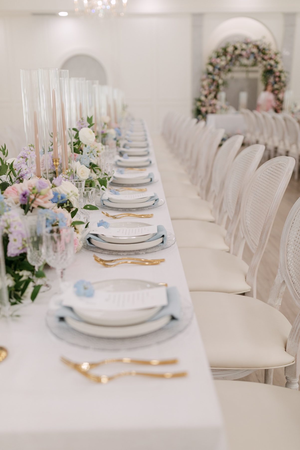 Looking down the length of the guest table, neat rows of chairs, plates, centrepieces and tapered candles.