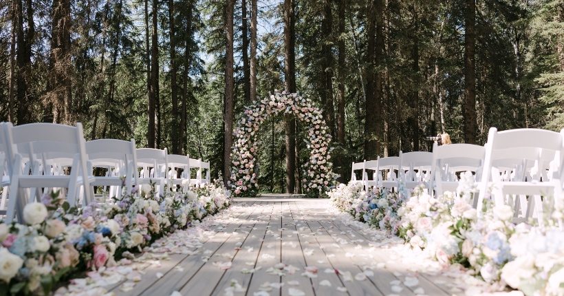 Looking down the aisle from a lower perspective, floral arrangements and petals lining the aisle and a massive, solid flower, pastel arch at the end.