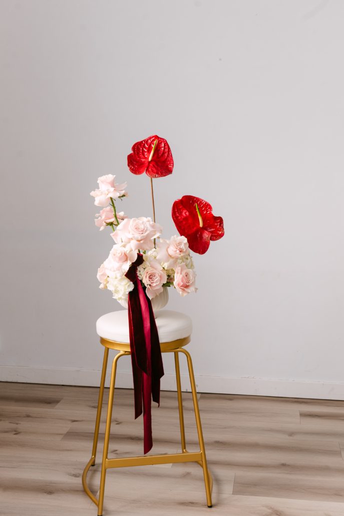 The Aria arrangement from our Valentine's Day collection, a front facing design in white, blush with bold red anthurium blooms and trailing burgundy velvet ribbons.