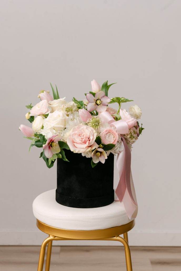 The Harper from our Valentine's Day collection, a lush arrangement of elegant white and blush blooms in a sophisticated black velvet hat box, accented with trailing ribbon.