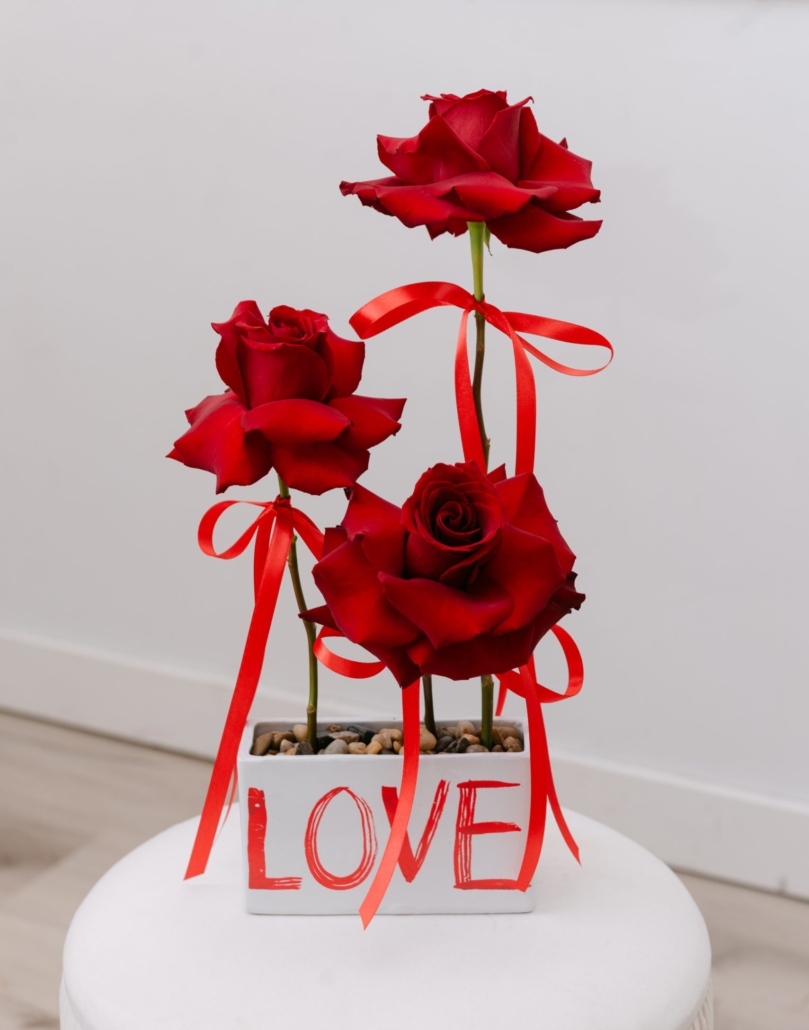 A Little Love arrangement from our Valentine's Day collection features 3 rich, velvety roses with reflexed petals and tied with red satin ribbon arranged in a white rectangular container.