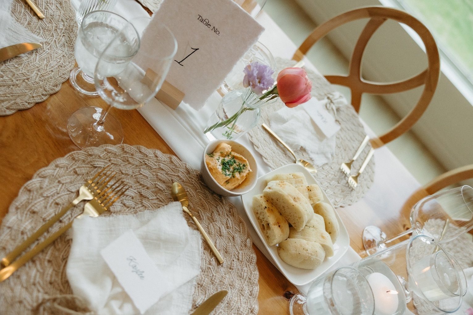 Place Setting One of the guest tables displayed with a table number, a bud vase with pink and purple blooms, and a plate of bread for the guests to share once they sit down.