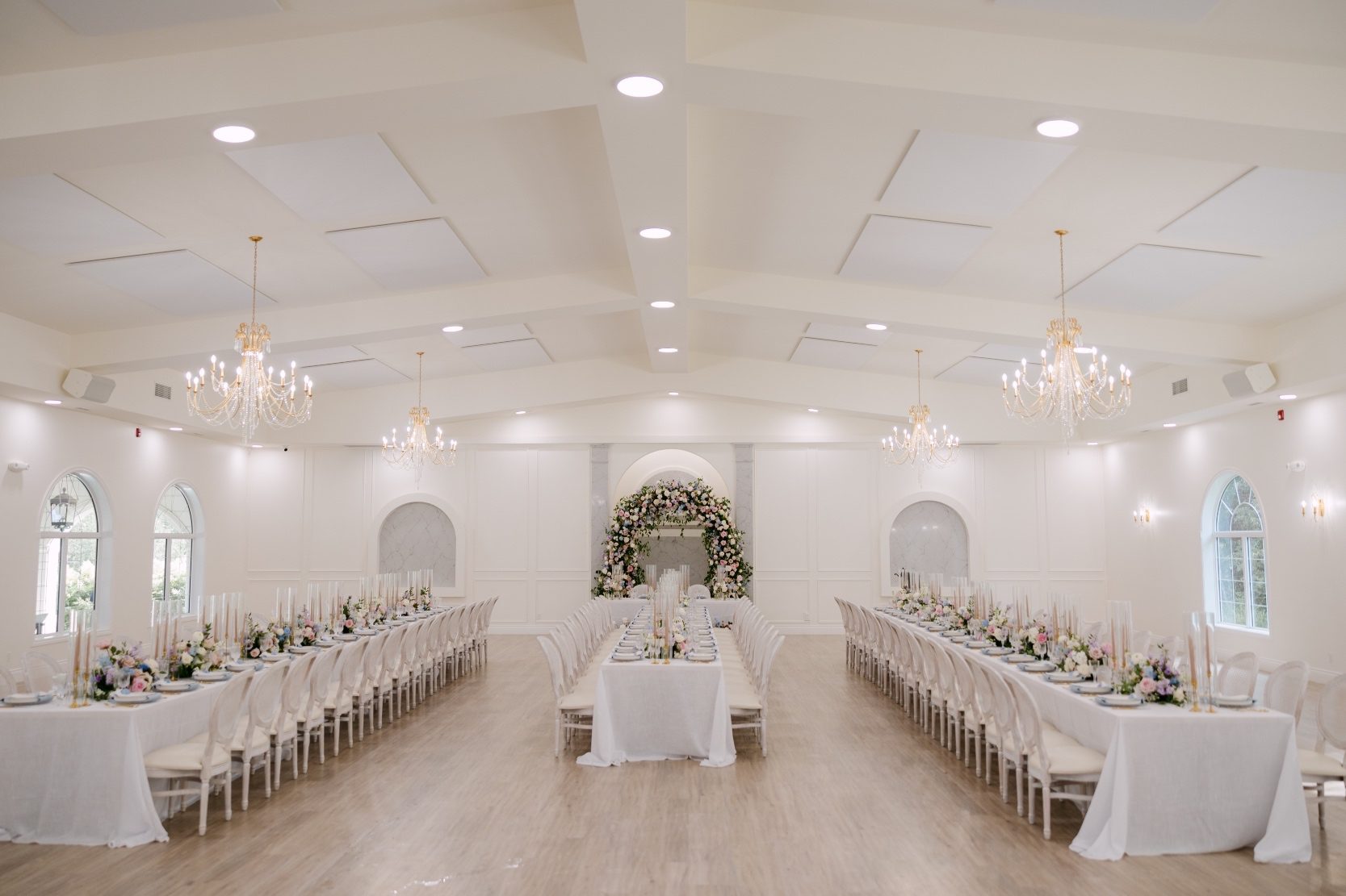 The reception space set up, with long rectangular tables for the guests, and a sweetheart table at the far end, highlighted by the floral arch.
