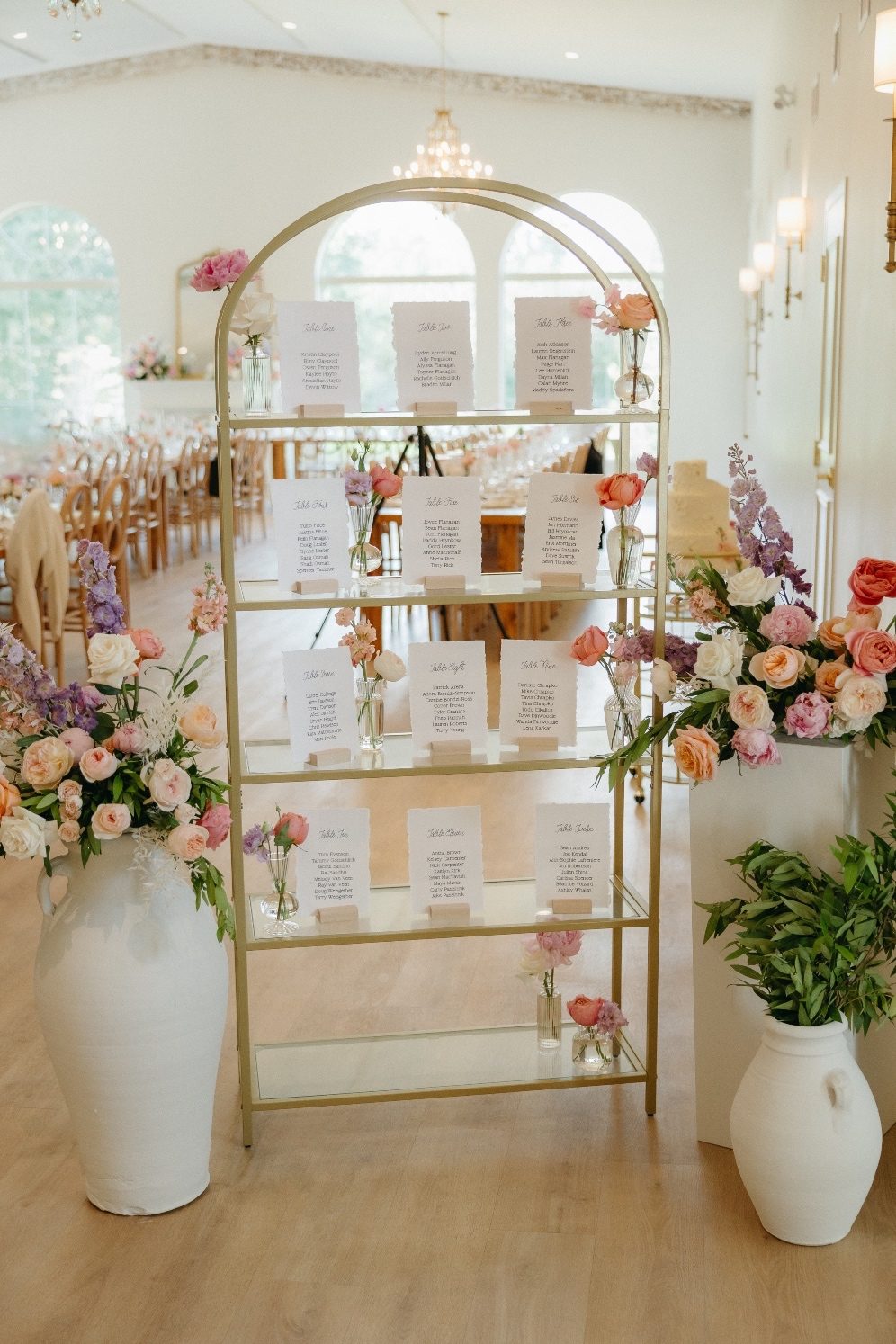 Seating Chart A gold + glass shelf displays the seating chart, with pastel bud vases tucked between the different tables cards. On either side the urns from the ceremony with big beautiful pastel arrangements.