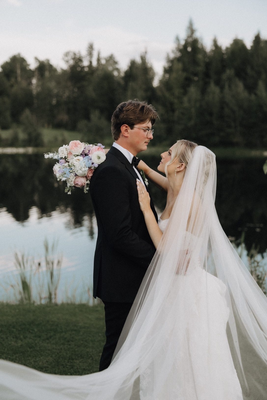 Oran and Kaylee facing each other in front of the pond, embracing like they may lean in for a kiss.