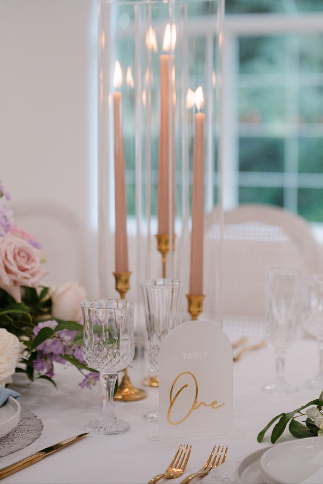 A grouping of three blush candles with a frosted acrylic and gold table number - the elevated details creating a perfectly cohesive look on the tables.