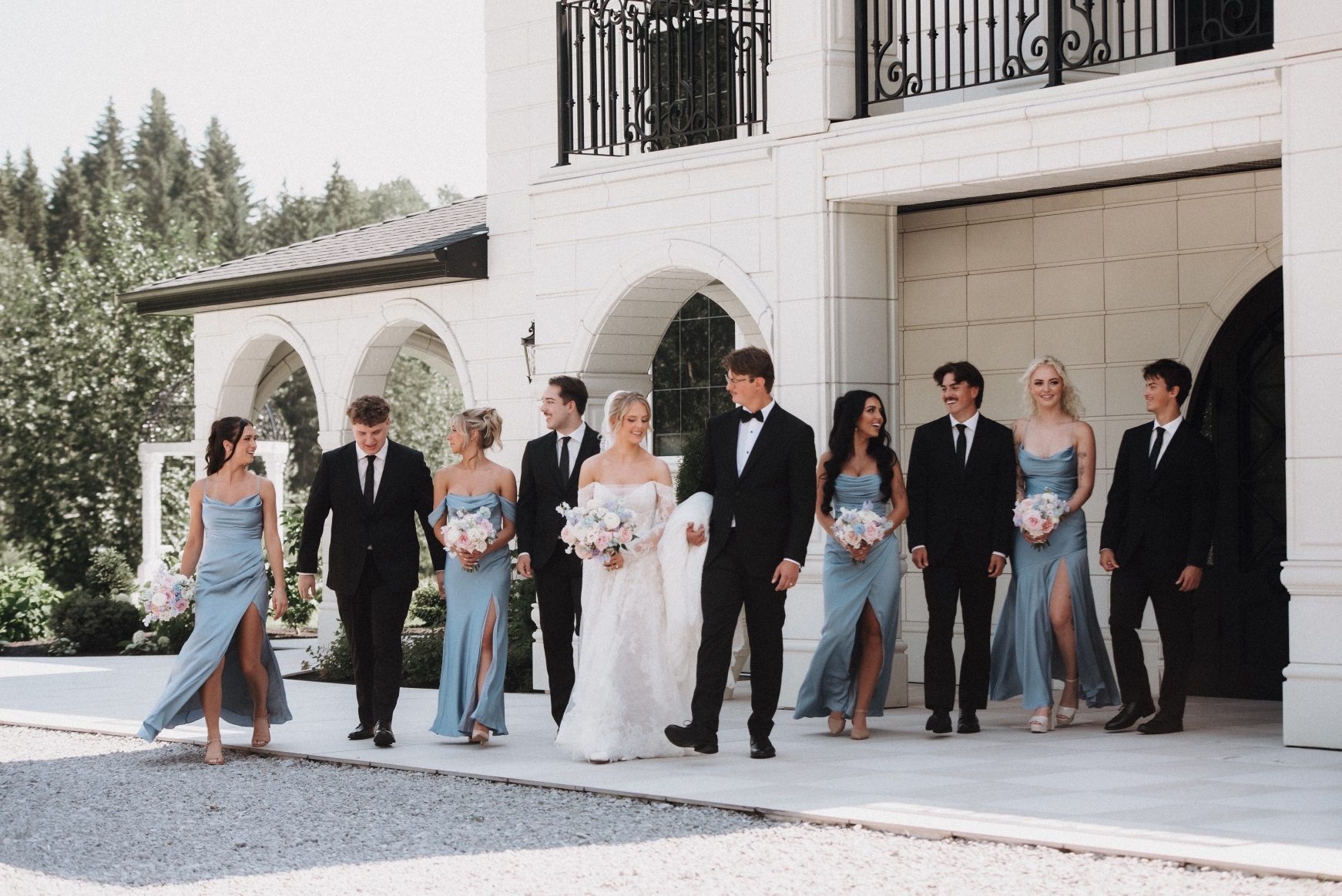 Oran, Kaylee and their wedding party are all walking outside of Archway Manor in pairs, chatting as they head off for more photos.