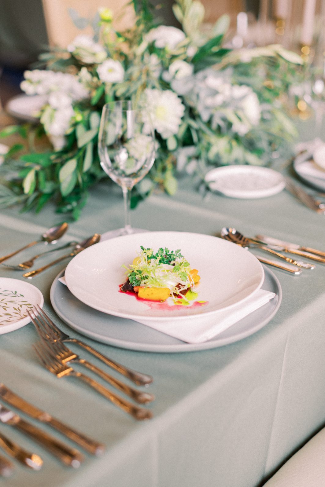 Appetizer Elegant plated wedding appetizer on a clean white plate set on sage table linens with gold flatware and white floral centrepiece.