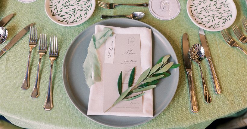 Feature An elegant place setting on sage linens, with a custom menu card accented with a sprig of olive branches.