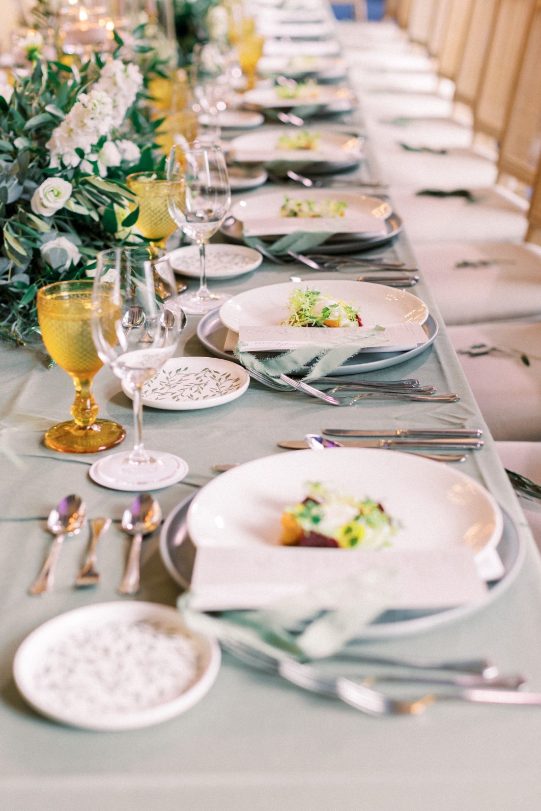 Guest Table Close up of wedding place settings with sage napkins, gold rimmed glassware, and lush floral centrepiece.
