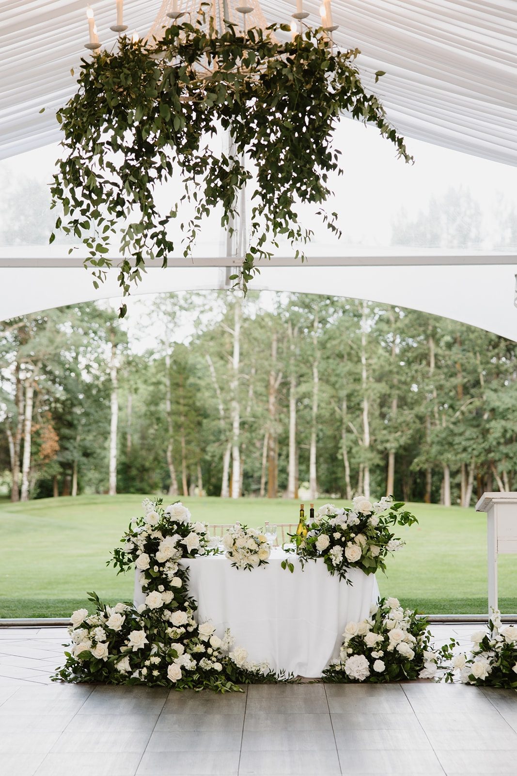 Tented Wedding reception at Hilltop wedding center featuring a chandelier with trailing beautiful luxury smilax and sweetheart table waterfall with white flowers, white roses