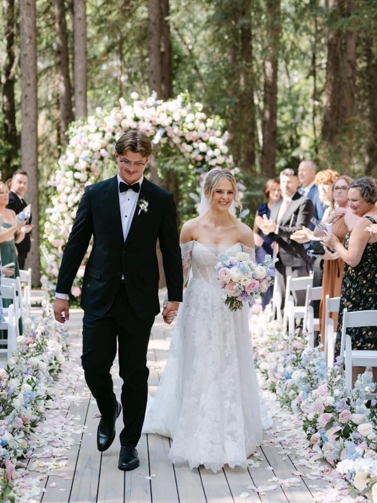 Grand luxury wedding ceremony with archway floral installation with garden roses in pastel tones of blush, pink, pale blue and lavender, light purple aisle hedges and bride and groom with bouquet at Archway Manor
