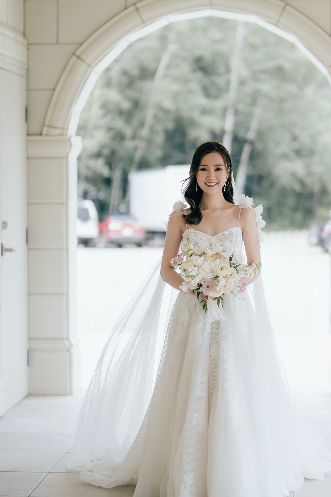 Gorgeous wedding bride in a wedding dress holding her bouquet designed with delicate pastel blooms in white and blush including ranunculus, butterfly ranunculus and garden roses at Archway Manor