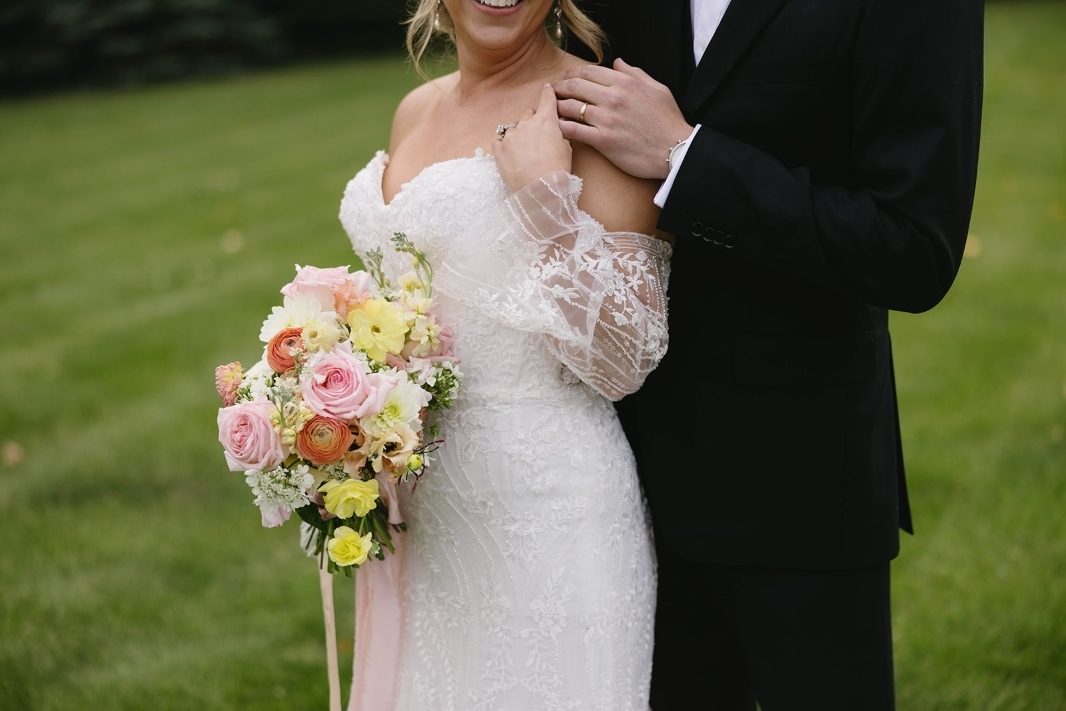 Groom and Bride and holding an loose and natural bridal bouquet of of spring bright pastels in yellow, peach coral pink and white with lush florals including gerbera daisy and hydrangea at Tangled Roots Venue