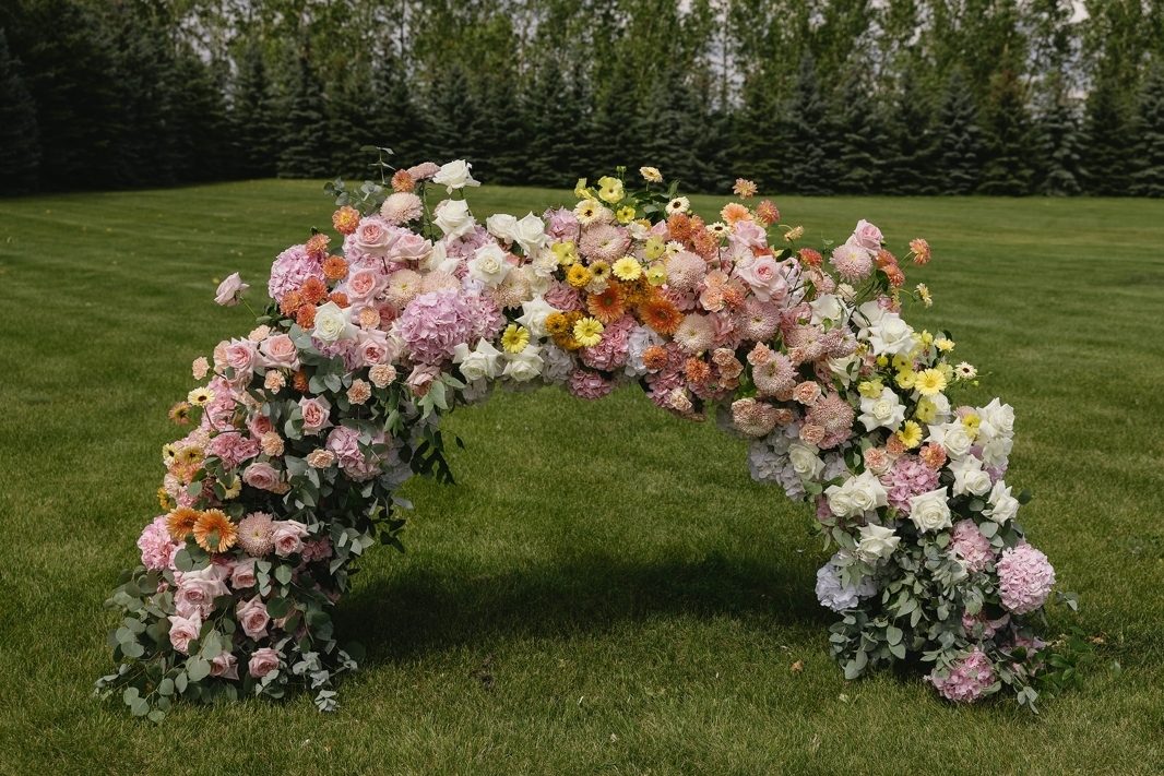 Wedding ceremony low arch designed in an ombre style of spring bright pastels in yellow, peach coral pink and white with lush florals including gerbera daisy and hydrangea at Tangled Roots Venue