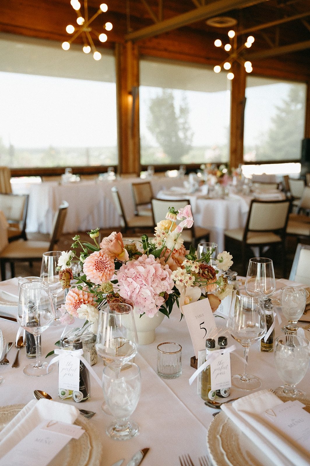 Beautiful Luxury centerpiece on a round table at a wedding reception with white tablecloth, and summer pastel flowers in peach, coral and yellow tones including hydrangea, dahlia, phlox, amd butterfly ranunculus