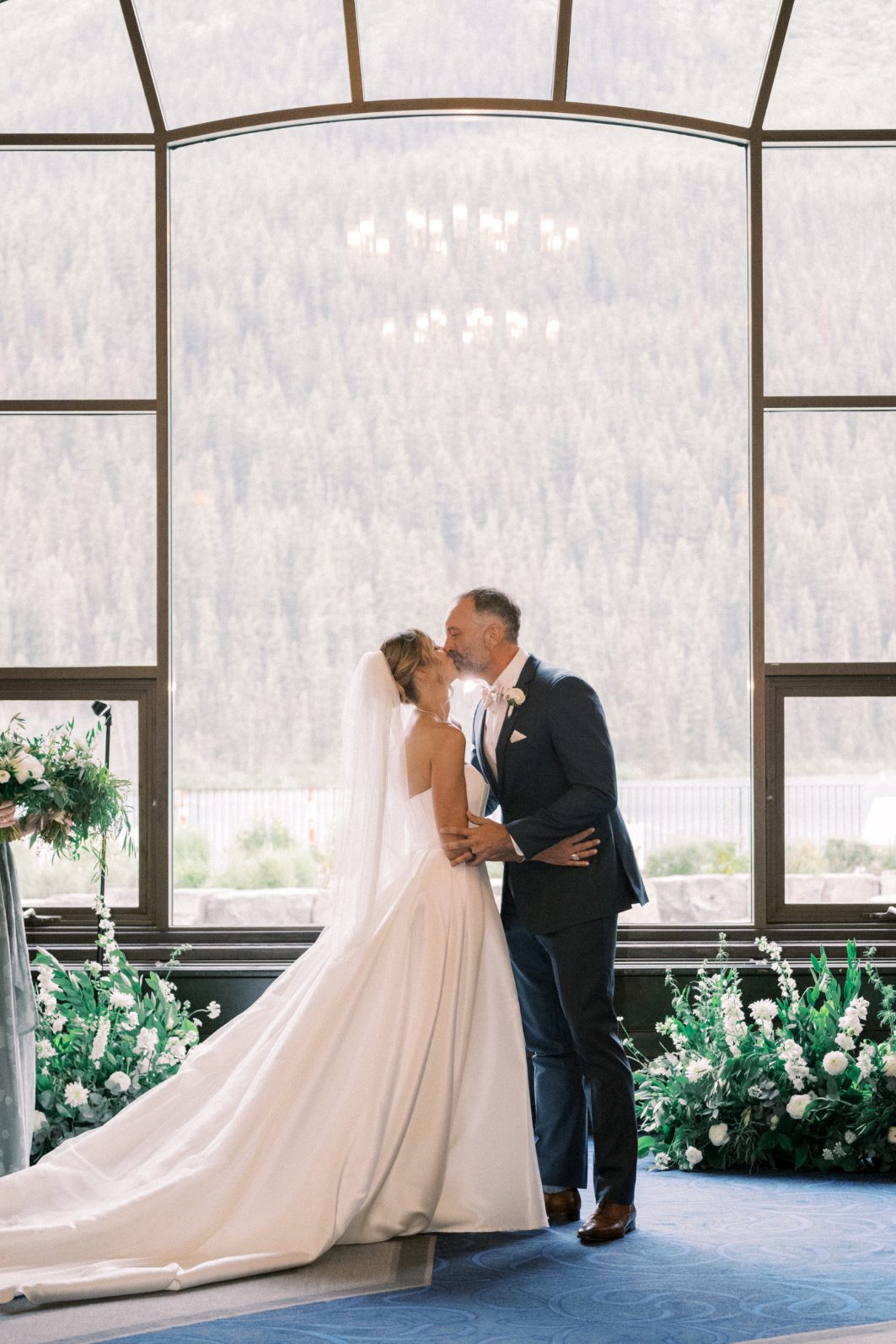 Kiss the Bride Bride and groom sharing a kiss in front of grand arched windows framed by a lush ground arch.
