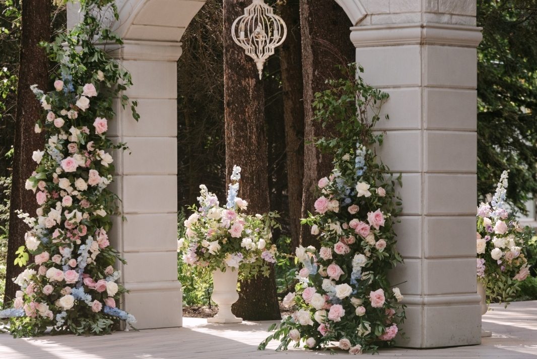 Beautiful luxury summer wedding ceremony design in pastel colors of blush, pale blue, lavender and white ar Archway Manor showing a broken arch placed against the stone archway and beautiful overflowing urn arrangements