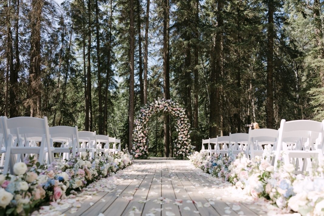 Grand luxury wedding ceremony with archway floral installation and full aisle hedge aisle markers and rose petal aisle with garden roses in pastel tones of blush, pink, pale blue and lavender, light purple aisle hedges and bride and groom with bouquet at Archway Manor