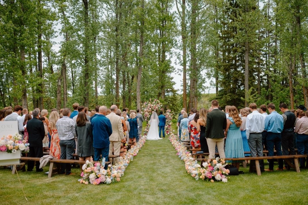 An outdoor spring wedding pipe archway and aisle hedge markers designed with bright pastel flowers including peonies, ranunculus, delphinium, tweedia, delphinium and lilacs and garden roses at 52 North Venue