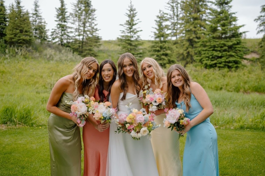 Bride and Bridesmaids at a spring outdoor wedding holding pastel bouquets designed with peonies, ranunculus, delphinium, tweedia and garden roses