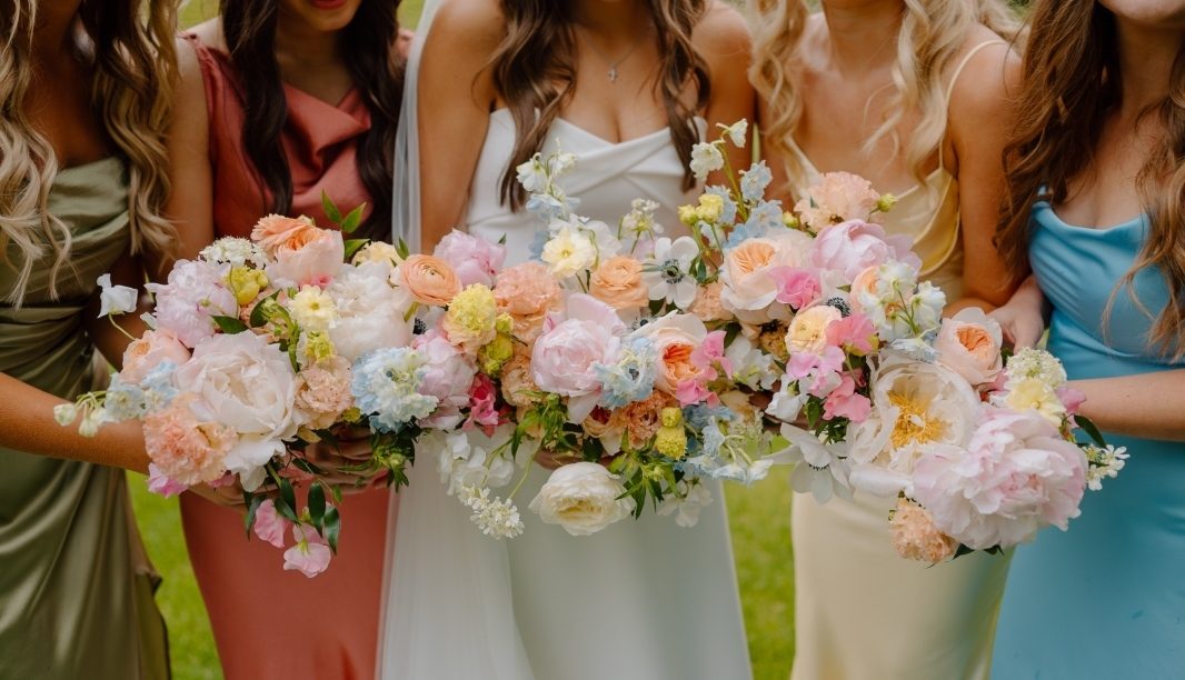 bride and bridesmaids at a spring wedding holding pastel bouquets designed with peonies, ranunculus, delphinium, tweedia and garden roses
