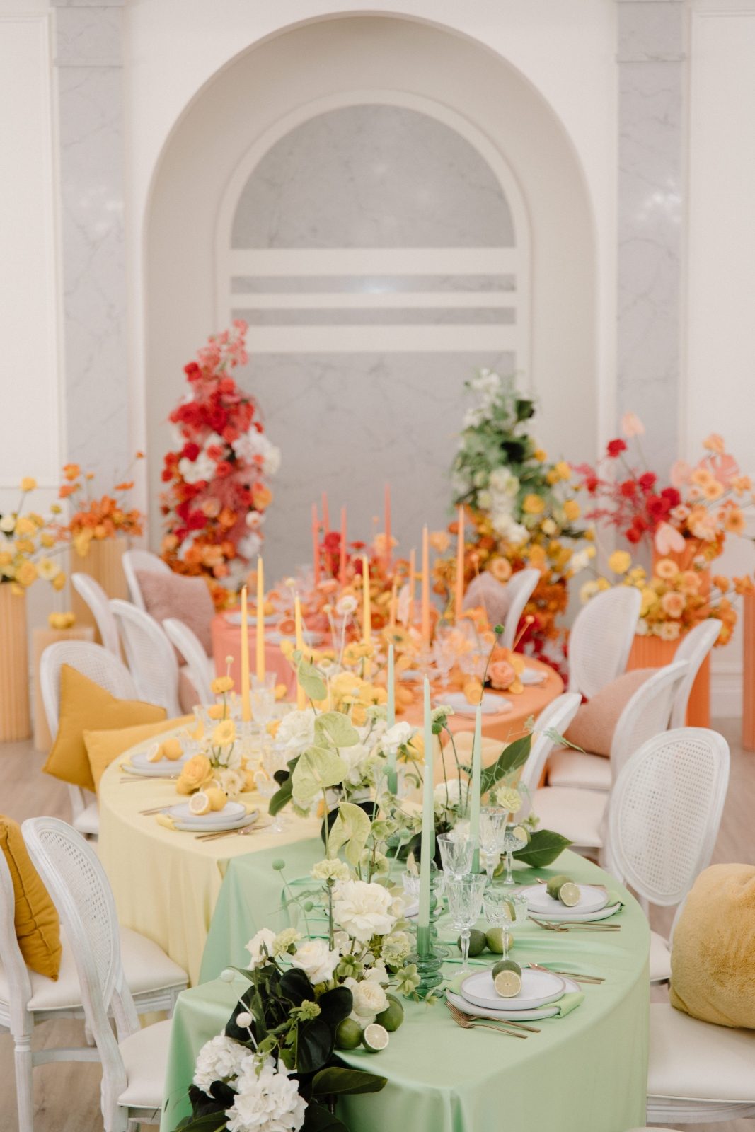 Colorbocked long serpentine table wedding flowers in bright citrus tones of green, orange, yellow, pink and coral with a table waterfall and pillar arrangements
