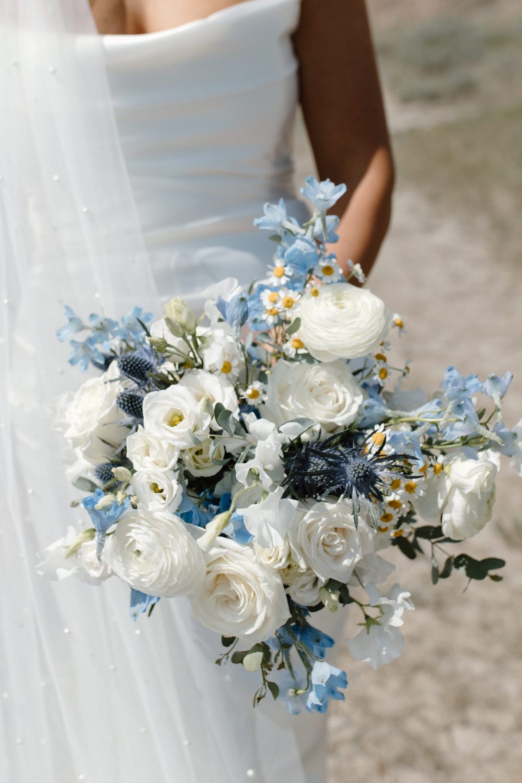 Bride with white and pale blue bouquet with roses ranunculus matricaria and delphinium