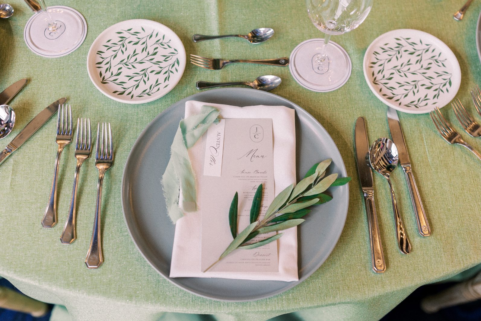 Place Setting Elegant wedding place setting with sage linens, custom menu, olive sprig detail, and refined silver flatware.