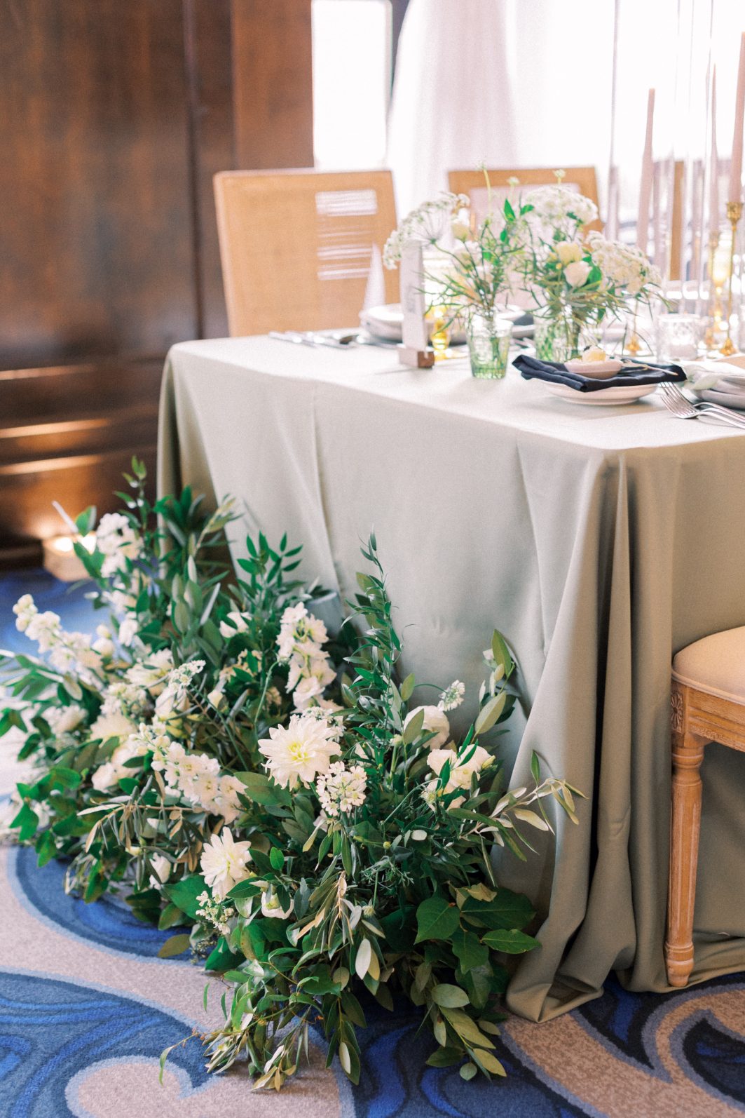 Reception Florals Table styled with soft sage linen and organic green and white wedding florals at the base.