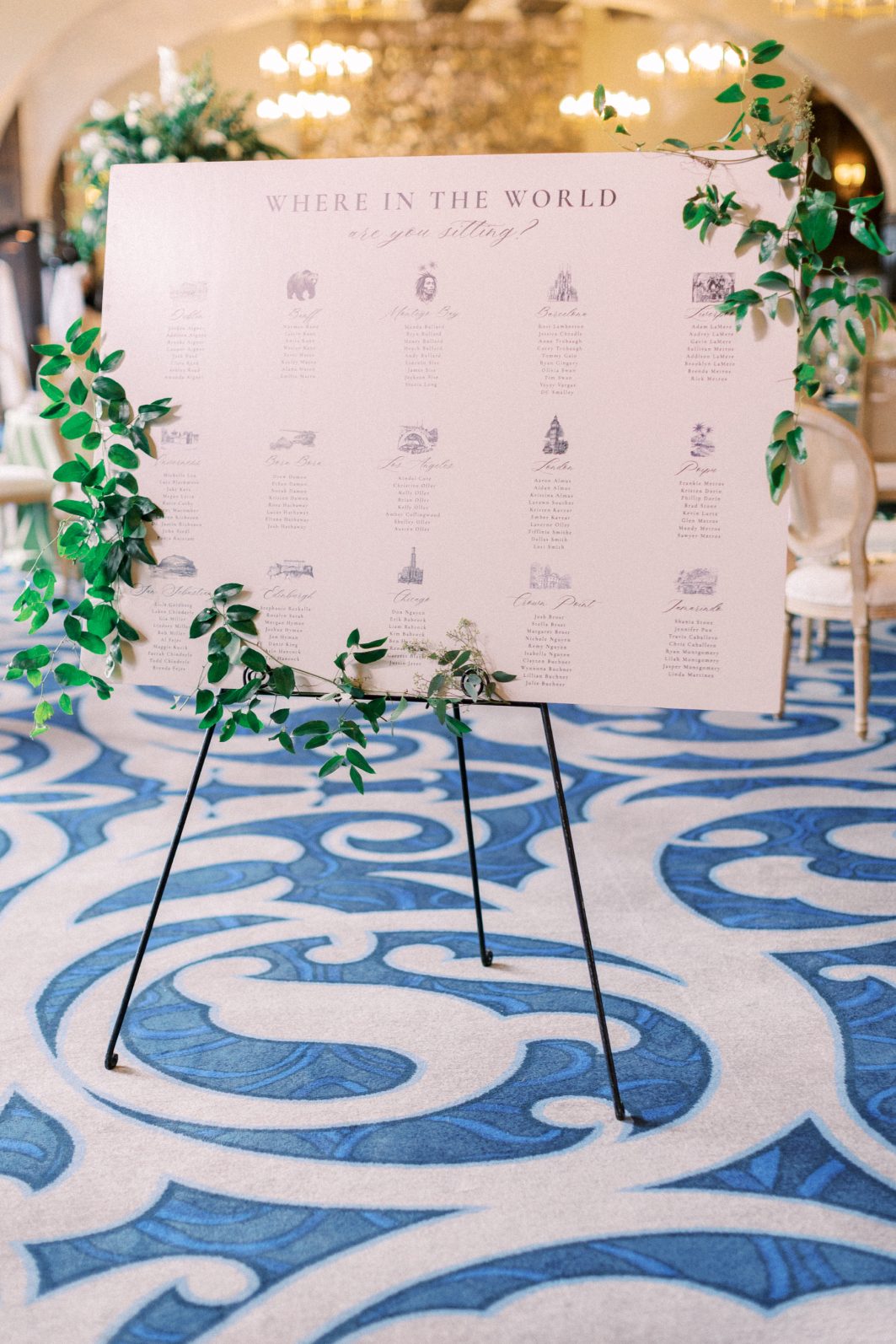 Seating Chart Custom wedding seating chart framed with fresh greenery in elegant ballroom reception space.