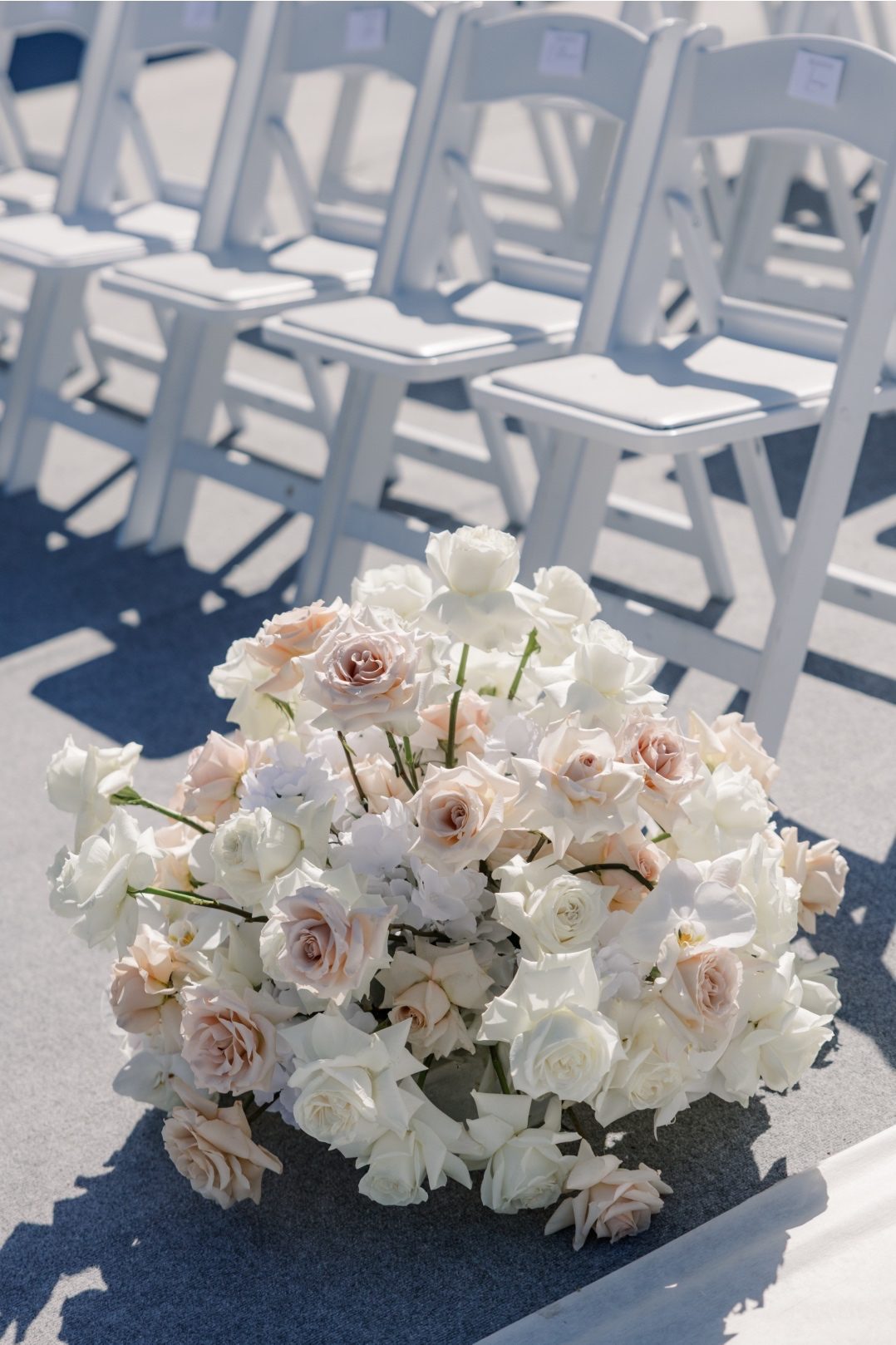 Aisle Arrangements Large floral arrangement of blush and white roses placed besides ceremony chairs on the terrace.