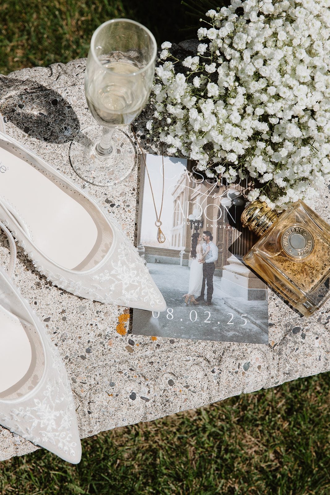 Cassidy + Adon White baby's breath bridesmaid bouquet paired along with a glass of champagne, the brides shoes and perfume.
