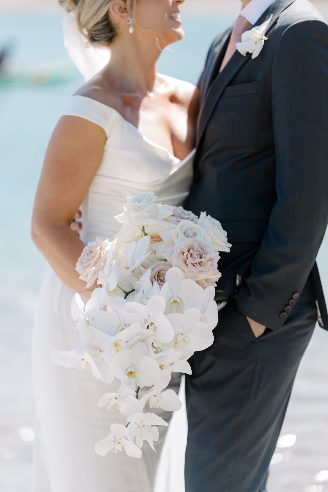 Bridal Bouquet Bride and groom standing by turquoise Lake Louise water, holding a cascading orchid and rose bouquet.