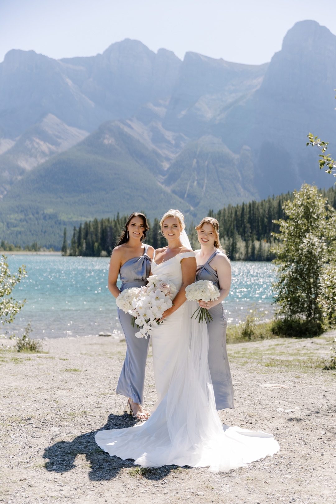 Bridal Party Bride and bridesmaids in soft blue dresses, posing by Lake Louise with mountains in the background.