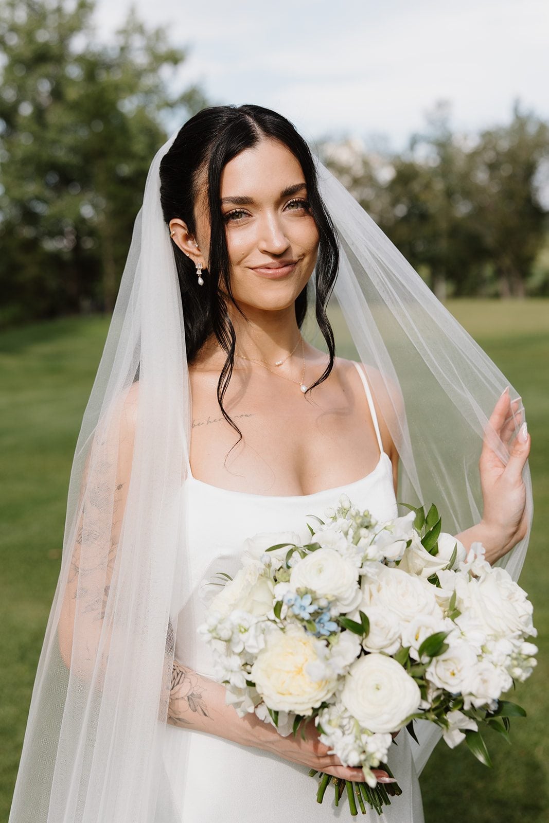 Cassidy + Adon Blushing bride holds a stunning white bridal bouquet of roses, ranunculus, sweet peas, tweedia and eucalyptus in one hand, while she running down her veil.