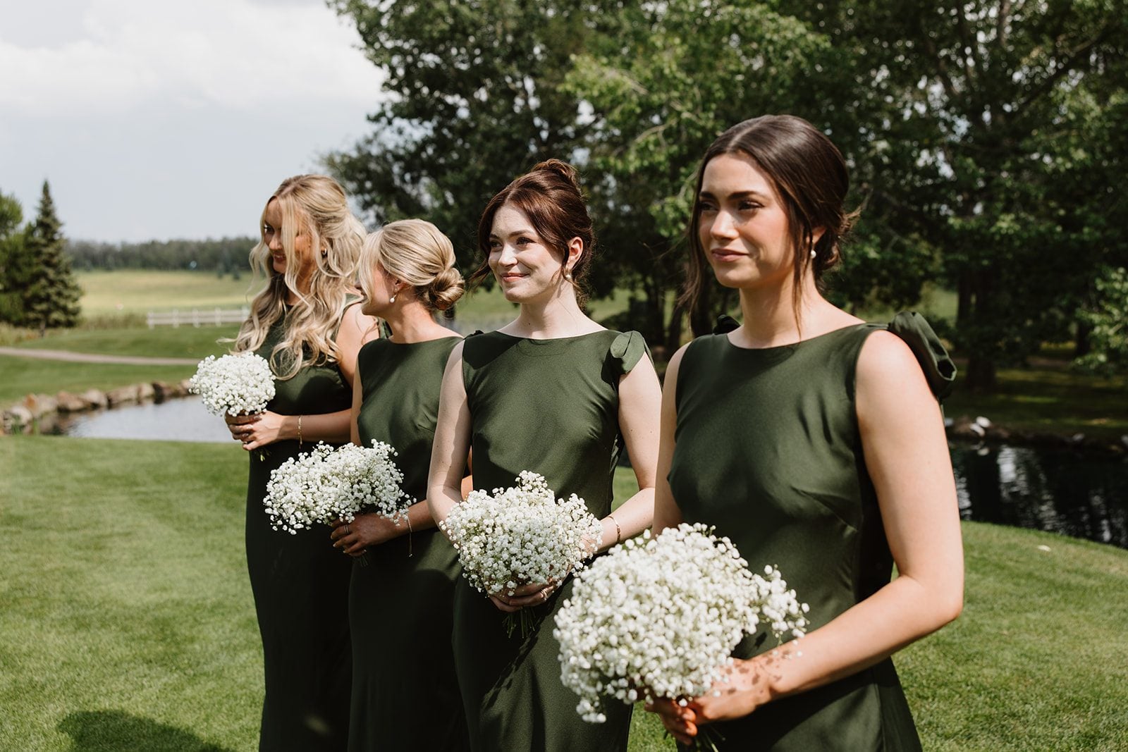 Cassidy + Adon At this green and white Hilltop Wedding Ceremony, the bridesmaids stand in a row wearing green satin dresses and holding white baby's breath bouquets.