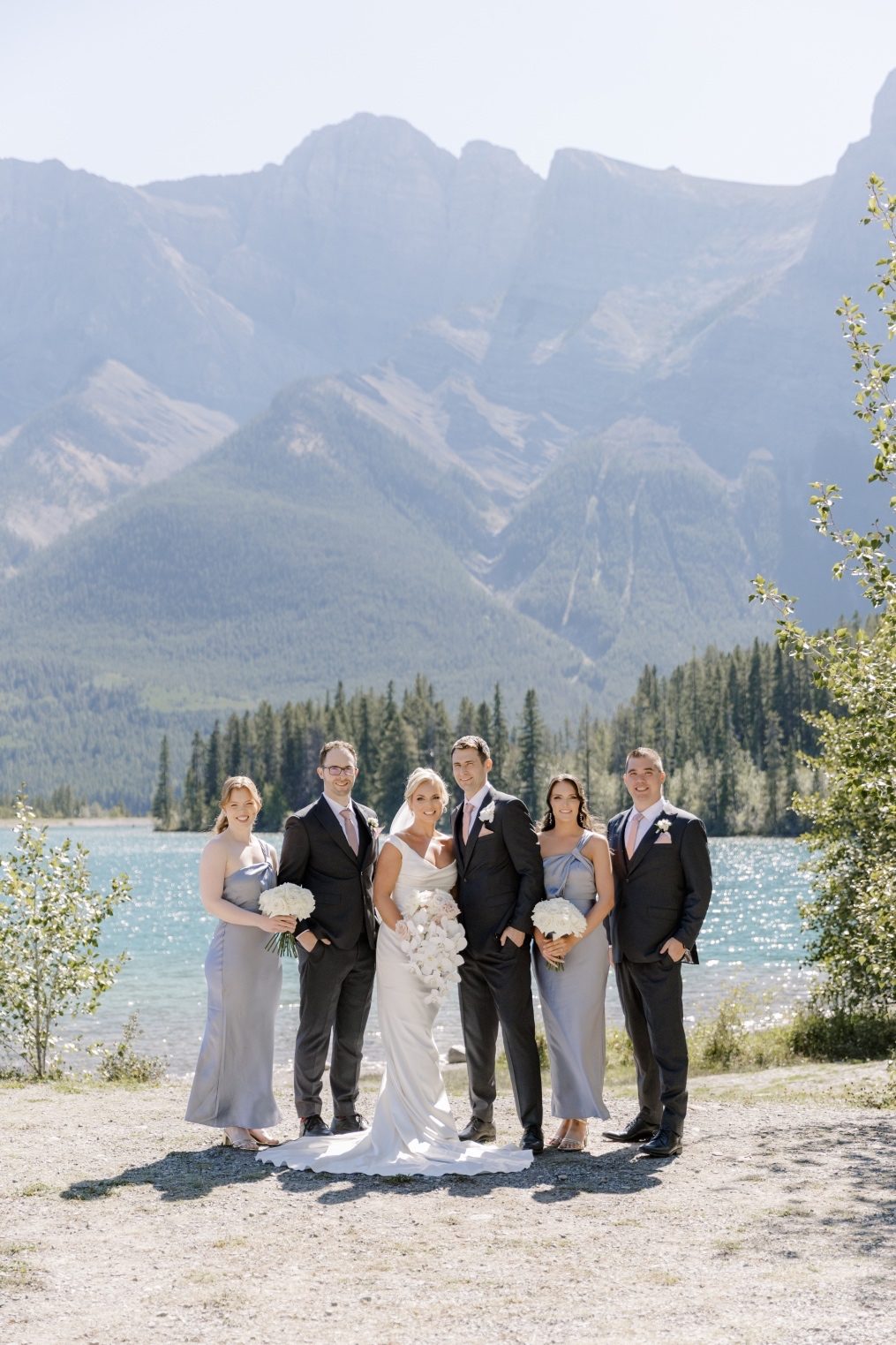 Calyx Wedding Party Wedding Party posing together in front of Lake Louise with dramatic mountain peaks behind them.